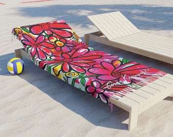 Könnte beinhalten: Ein Strandtuch mit einem auffälligen Blumenmuster in Rot-, Rosa-, Gelb- und Grüntönen. Das Tuch liegt auf einer Holzliege an einem Sandstrand. Ein Volleyball liegt daneben.