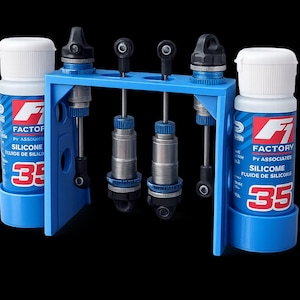 May include: A blue stand holding four silver and blue shock absorbers, with two bottles of silicone fluid. The bottles have white caps and blue labels with the text "FACTORY" and "SILICONE". The number "35" is prominently displayed.