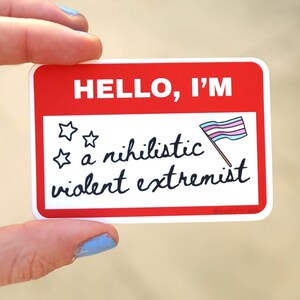 May include: A rectangular sticker with a red border and the words "HELLO, I'M" in white. Below, it reads "a nihilistic violent extremist" in black script, with star and flag illustrations.