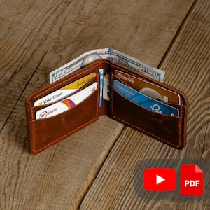 Puede incluir: Cartera de cuero marrón abierta con múltiples ranuras para tarjetas y efectivo. La cartera está llena de tarjetas de crédito y billetes de cien dólares estadounidenses. El cuero tiene un aspecto envejecido.