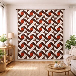 May include: Large wall hanging with a geometric pattern in shades of brown, white, and rust. The design features repeating zig-zag lines and square and triangular shapes. The textile is displayed in a living room setting.