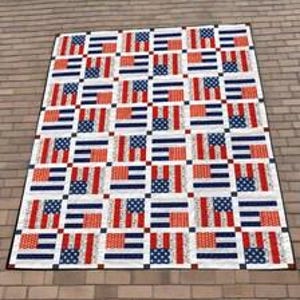 May include: A rectangular quilt featuring a repeating pattern of American flag motifs. The design consists of alternating blocks of red, white, and blue stripes and stars, separated by small white squares, finished with a thin dark blue border.