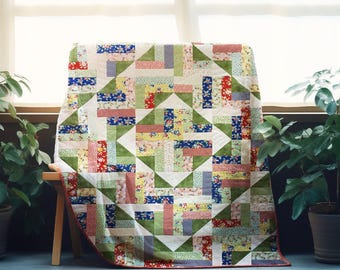May include: A patchwork quilt with a geometric design in shades of red, blue, green, and yellow. The quilt is made from various floral and patterned fabrics. It is draped over a small wooden bench, in front of a window.