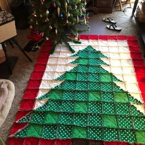 May include: A handmade Christmas tree quilt. The quilt features a green tree design with white polka dots on a white background, framed by a red border. The quilt is approximately 60 inches long and 48 inches wide.