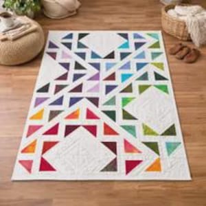 May include: A rectangular quilt featuring a white background with a geometric pattern of multicolored triangles in shades of red, orange, yellow, green, blue, and purple. The fabric displays intricate quilted stitching throughout the surface.