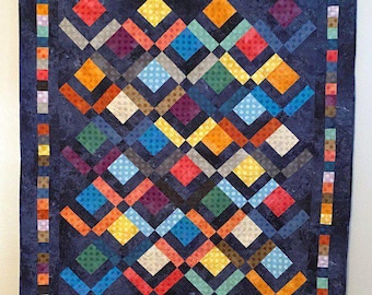 May include: A handmade quilt with a dark blue background and a colorful geometric pattern. The quilt features a repeating diamond design in shades of red, orange, yellow, green, blue, and purple. The border is a patchwork of small, colorful squares.