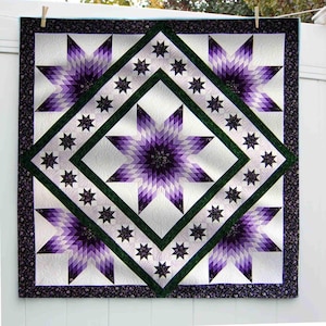 May include: A handmade quilt featuring a central star design in shades of purple, surrounded by a green diamond and smaller star accents. The quilt has a white background and a floral patterned border. It is hanging on a white fence.