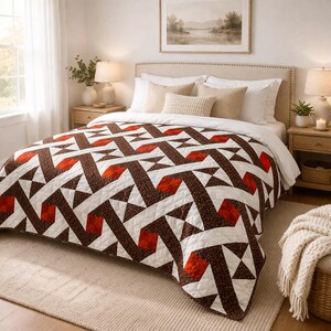 May include: A geometric patterned quilt in shades of brown, white, and red covers a bed. The quilt features a repeating design of triangles and rectangles. The bed is in a well-lit bedroom with neutral tones.