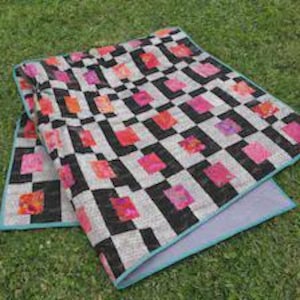 Peut inclure: Une couverture matelassée présentant un motif géométrique de rectangles noirs et de carrés blancs, agrémentée de petits carrés aux motifs floraux rose vif et orange. La courtepointe est finie avec un biais bleu clair sur les bords.