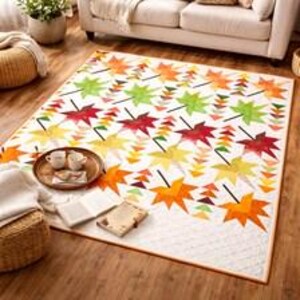 Könnte beinhalten: Ein rechteckiger Quilt mit einem sich wiederholenden Muster aus Herbstblättern in Rot-, Orange-, Gelb- und Grüntönen auf weißem Grund. Das Design umfasst kleine dreieckige Akzente und einen dünnen orangefarbenen Rand auf einem Holzboden.