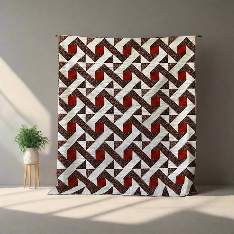 May include: A large quilt with a geometric pattern of white, brown, and red shapes. The quilt is hanging against a neutral wall, showcasing its intricate design. The pattern features interlocking shapes and triangles.