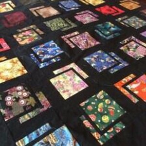 May include: A quilt featuring a grid of multicoloured fabric squares separated by black sashing. The squares display various patterns including floral, geometric, and scenic prints in shades of red, blue, green, yellow, and purple.