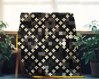 Può includere: Una trapunta nera e grigia con un motivo ripetuto di croci bianche e gialle. La trapunta è drappeggiata su una panca di legno, con un bordo giallo. Il design della trapunta presenta un patchwork di quadrati in varie tonalità di grigio e nero.
