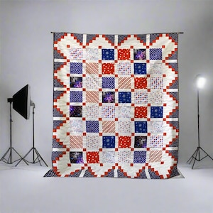May include: A large, square quilt with a patchwork design in red, white, and blue. The quilt features squares with various patterns, including stripes, polka dots, and fireworks. The border is a scalloped design with a navy blue polka dot pattern.