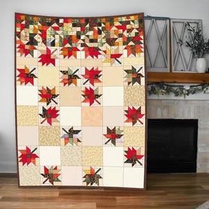 May include: A large, handmade quilt with a fall theme. The quilt features a patchwork design with squares and maple leaf patterns in shades of red, orange, brown, and beige. The quilt is displayed against a neutral background.