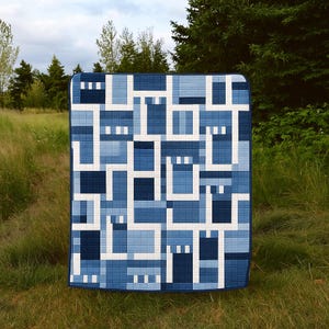 Könnte beinhalten: Eine blau-weiße Steppdecke mit einem geometrischen Muster. Die Steppdecke hat ein Patchwork-Design mit Quadraten und Rechtecken in verschiedenen Blau- und Weißtönen. Die Steppdecke wird im Freien in einem grasbewachsenen Bereich gezeigt.