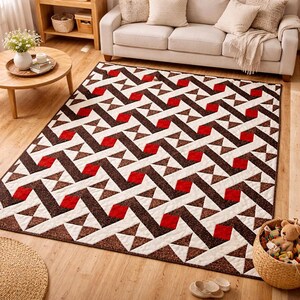 May include: A rectangular area rug with a geometric pattern. The design features repeating shapes in brown, red, and white. The rug is placed on a wooden floor in a living room setting. A sofa and coffee table are visible in the background.