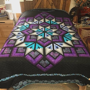 May include: A handmade quilt with a starburst design in shades of purple, teal, grey, and white on a black background. The quilt features geometric patterns and a decorative border.