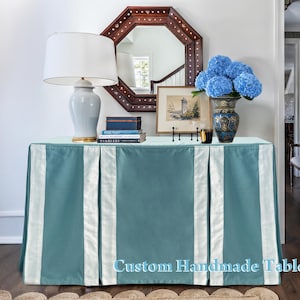 May include: A teal custom handmade tablecloth with white vertical panels. The table is decorated with a lamp, books, a mirror, a framed picture, a vase of blue flowers, and a candle. The tablecloth is made of a soft, luxurious fabric.