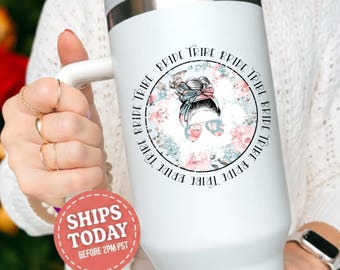 May include: White tumbler with a handle, featuring a floral design and the words "Bride Tribe" in a circular pattern. The design includes an illustration of a woman with sunglasses and a bun. The tumbler has a silver rim.