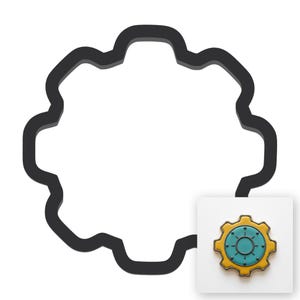May include: A black gear-shaped cookie cutter outline positioned next to a small square image of a finished gear-shaped cookie with a yellow outer rim, a teal center, and a circular design with small dots around the inner edge.