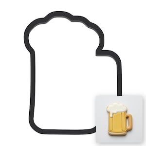 Puede incluir: Un cortador de galletas negro con forma de jarra de cerveza junto a una baldosa blanca cuadrada que muestra una galleta decorada con forma de jarra, con líquido amarillo, asa marrón y espuma de glaseado blanco escurriendo por el lado.