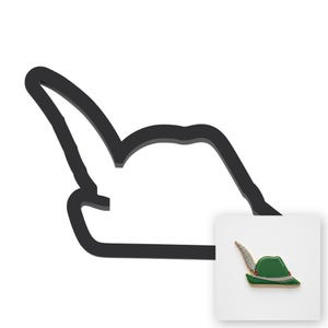 May include: A black outline of a Tyrolean hat with a feather and a small enamel pin of a green Tyrolean hat featuring a grey feather, a white band, and a red accent detail. The pin is positioned in the lower right corner of the black hat outline.