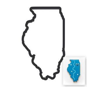 Op de afbeelding: Een zwarte metalen koekjesvorm in de vorm van de staat Illinois. Een klein, kleurrijk koekje in de vorm van Illinois wordt in de hoek getoond. De koek is blauw met witte sterren en een lachend gezicht.