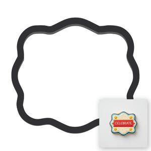 May include: A black, cloud-shaped cookie cutter with a small, rectangular cookie that says "CELEBRATE". The cookie has a red banner with white text, yellow stars, and a blue border. The cutter is made of plastic.