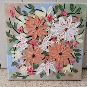 May include: A square canvas painting featuring a textured floral arrangement with thick impasto brushstrokes. The composition includes peach, white, and small pink flowers with dark green leaves and stems against a soft, multi-colored pastel background.