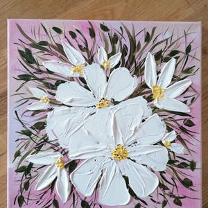 May include: Square canvas art featuring a textured, impasto painting of white flowers with yellow centers. The flowers are set against a pink background with green foliage. The artwork is a close-up of the flowers.