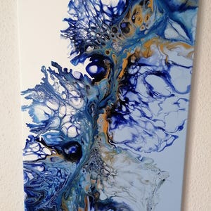 Könnte beinhalten: Abstrakte Acrylmalerei auf Leinwand. Das Kunstwerk zeigt ein fließendes Design mit Blautönen, Weiß und goldenen Akzenten. Das Gemälde hat eine dynamische, fließende Komposition mit einer Mischung aus Texturen und Mustern.