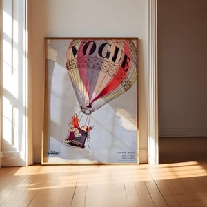 May include: A framed vintage Vogue magazine cover. It depicts a colourful hot air balloon with the word "VOGUE" at the top. A person is in the basket below. The words "Summer Travel" are also visible on the poster.