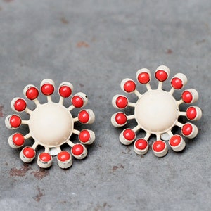 Może przedstawiać: Para białych i czerwonych kolczyków w kształcie kwiatu. Każdy kolczyk ma białe centrum i 12 czerwonych koralików wokół krawędzi.