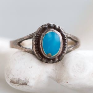May include: A silver ring with a turquoise stone set in a bezel setting. The ring has a simple band with a split design.