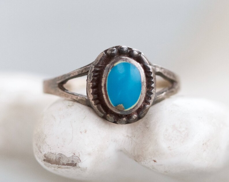 May include: A silver ring with a turquoise stone set in a bezel setting. The ring has a simple band with a split design.