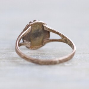 May include: A silver ring with a round, oval-shaped stone set in the center. The ring is simple and elegant.