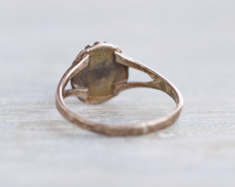 May include: A silver ring with a round, oval-shaped stone set in the center. The ring is simple and elegant.