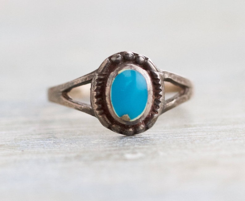 May include: A silver ring with a turquoise stone set in a decorative bezel. The ring has a simple band with a split design.