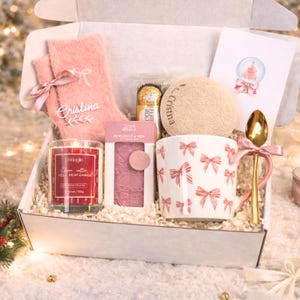 Può includere: Una scatola regalo contenente un paio di calzini rosa soffici con un nastro, un cioccolatino Ferrero Rocher, un sottobicchiere rotondo beige con il nome Cristina, una tazza bianca con fiocchi rossi, un cucchiaio dorato, una candela rossa e un biglietto.