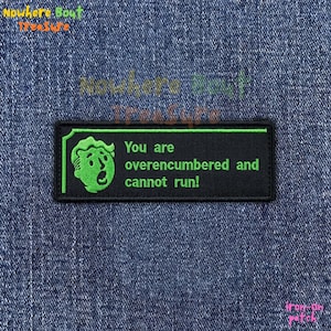 May include: Black rectangular iron-on patch with a green outline and text. The patch features a green cartoon face and the words "You are overencumbered and cannot run!" on a denim background.