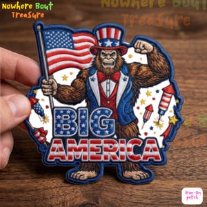 May include: Embroidered patch featuring a Bigfoot-like creature in patriotic attire, holding an American flag. The patch includes the text "BIG AMERICA" in red, white, and blue, with additional firework and star details. The patch is designed to be ironed on.