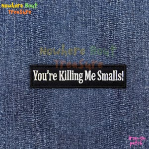 May include: A black rectangular iron-on patch with the phrase "You're Killing Me Smalls!" in white lettering. The patch is set against a blue denim background.