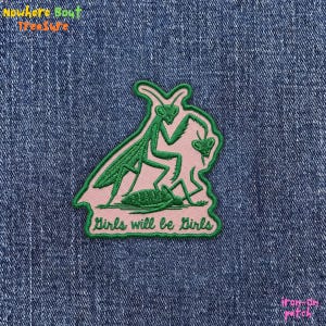 May include: Embroidered patch featuring a green praying mantis design on a pink background. The patch includes the text "Girls will be Girls" in green. The patch is iron-on.