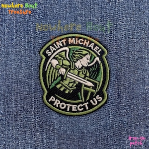 May include: Embroidered patch featuring Saint Michael, depicted with a sword and shield, surrounded by the text "Saint Michael Protect Us." The patch has a green, black, and white color scheme.