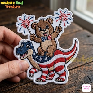 May include: Embroidered patch featuring a brown bear riding a dinosaur decorated with the American flag. The bear holds sparklers with red, white, and blue fireworks. The patch has the text "Nowhere Bout Treasure" and "iron-on patch".