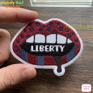 May include: Embroidered patch in the shape of lips, featuring a red and blue color scheme with stars and stripes. The word "LIBERTY" is embroidered in white across the center. The patch is an iron-on.