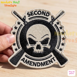 May include: Embroidered patch featuring a skull with crossed rifles, surrounded by stars. The words "SECOND AMENDMENT" are arched above and below the skull. The patch is black, white, and beige.