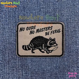May include: An iron-on patch with a raccoon illustration holding a knife. The patch has the text "NO GODS NO MASTERS BE FERAL" in black font. The patch is rectangular with a tan background and black border.