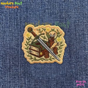 May include: Embroidered patch featuring a sword, books, and art supplies. The patch has a cream-colored border with a floral design. The sword is silver, and the books are green and brown. The patch has the text "iron-on patch".